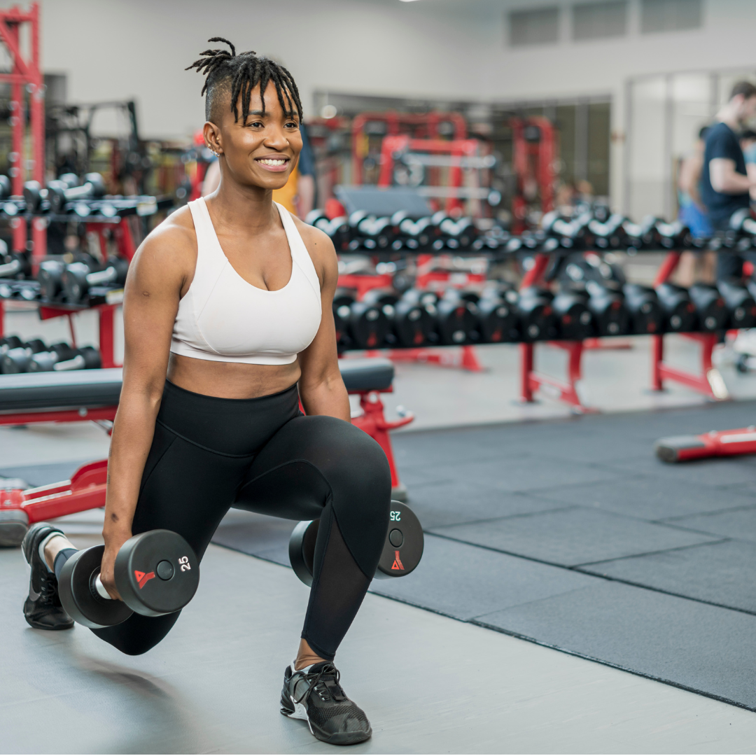 Smiling woman performing a goblet squat holding a dumbbell in a gym, participating in a strength training program for menopause support.