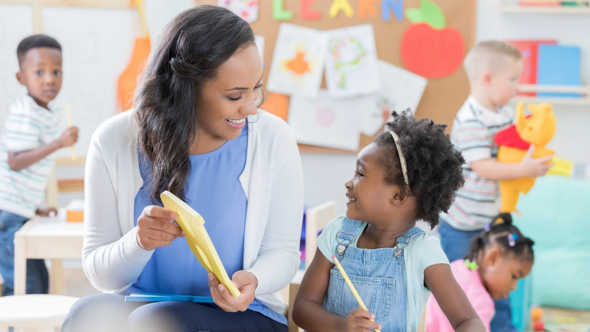 An Early Childhood Educator helps a young girl learn to write at a child care centre