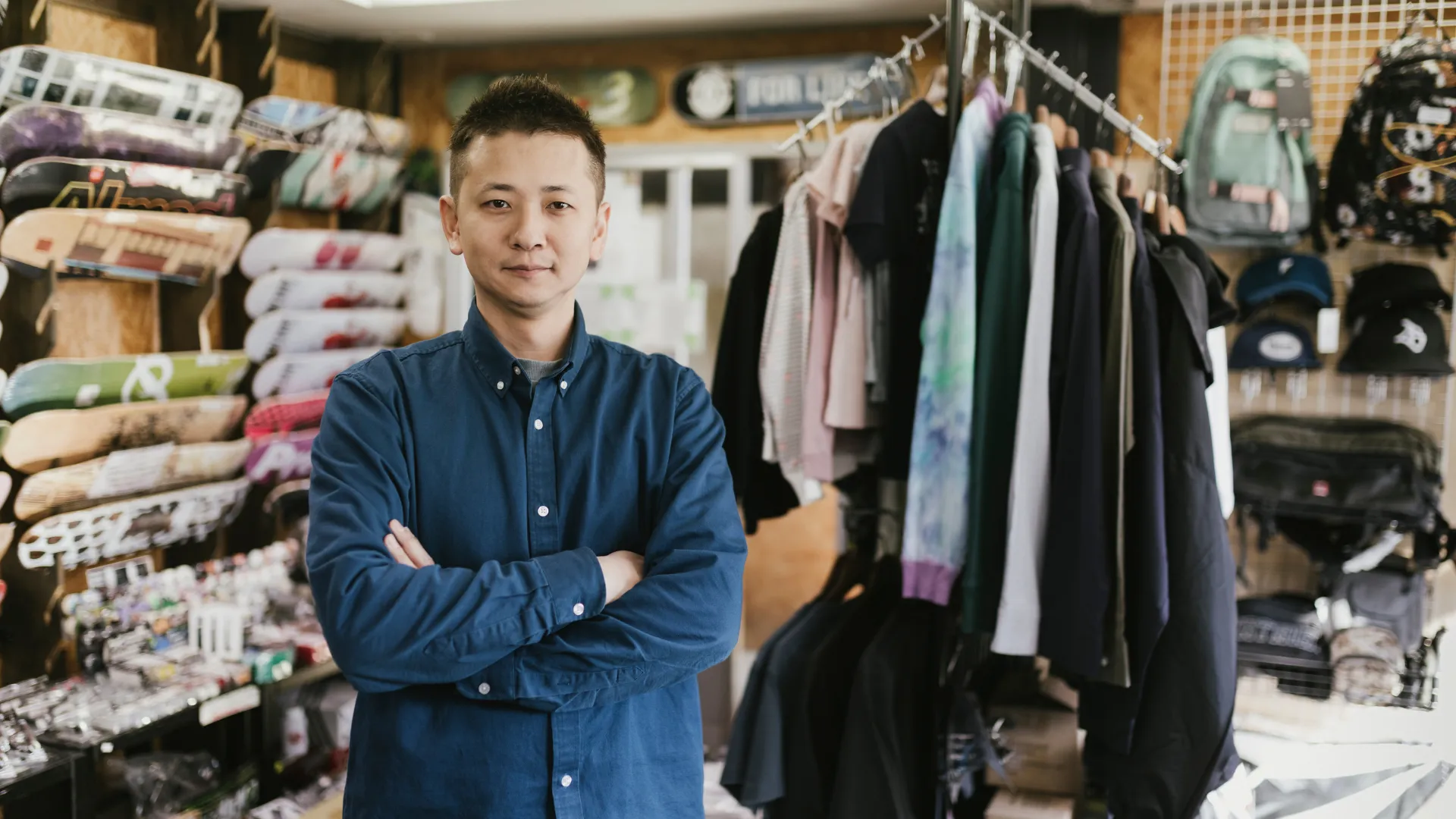 A skate shop owner stands in front of boards and apparel in their store