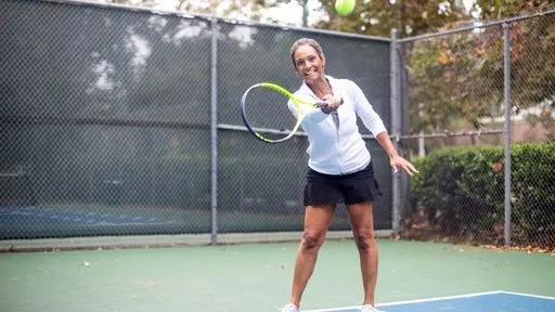 A woman smiles while hitting a tennis ball with a racquet on an outdoor tennis court