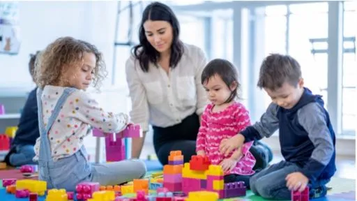 A young woman oversees a group of four children playing on the floor with blocks in a child care centre
