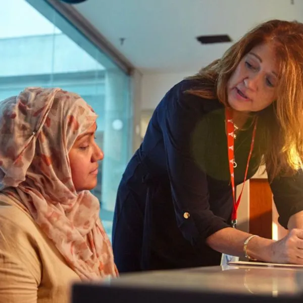 A YMCA program coach standing at a desk interacts with a female participant who is sitting