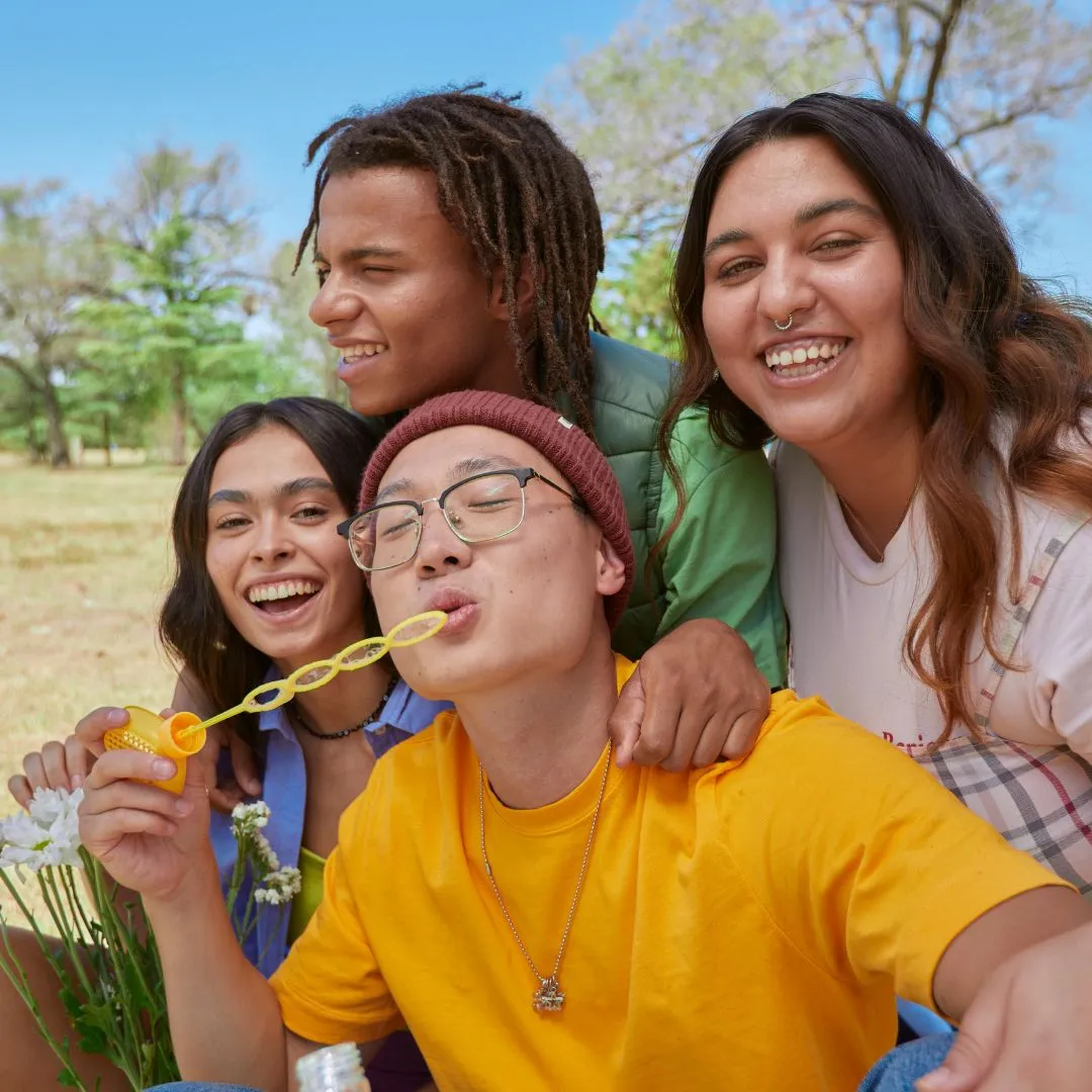 Four diverse young adults smile and blow bubbles