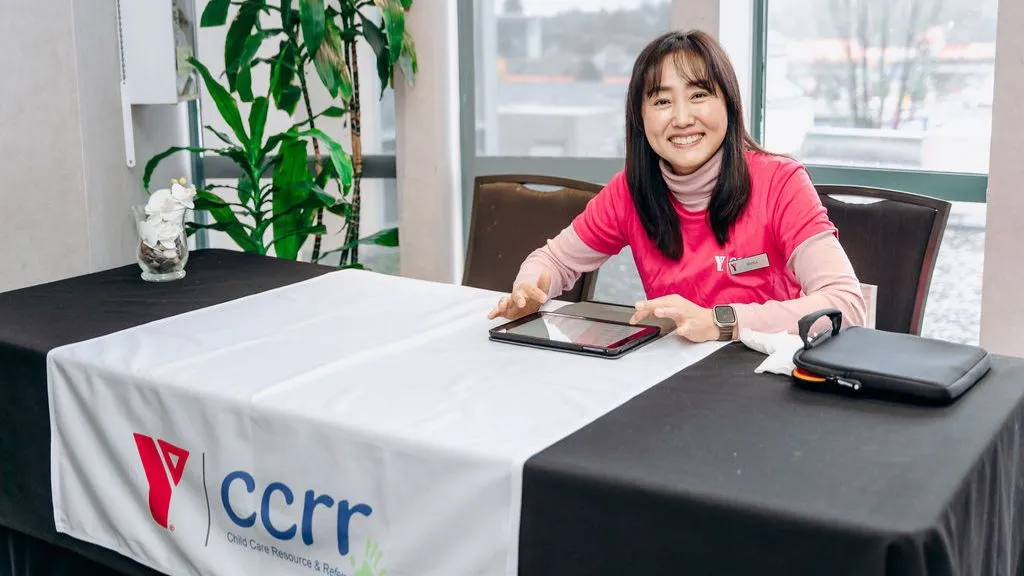 A smiling YMCA CCRR staff team member sits at an event check-in table