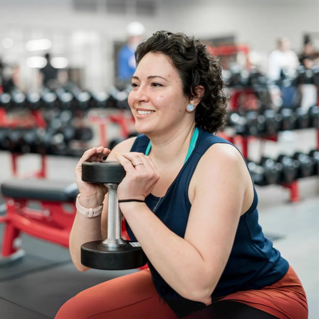 Smiling woman performing a goblet squat holding a dumbbell in a gym, participating in a strength training program for menopause support.