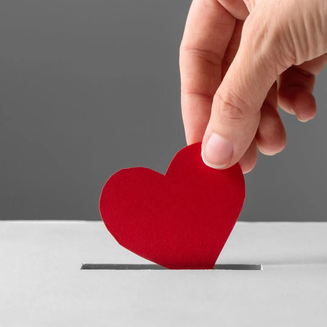 A hand drops a paper heart into a donation box