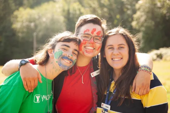 Three young women serving as YMCA Camp Elphinstone counsellors, posing for a photo with painted faces.