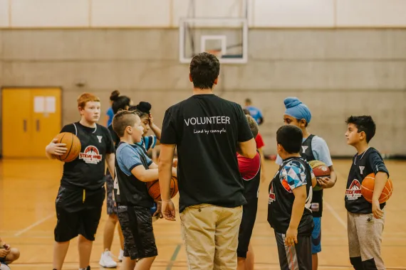 A volunteer basketball coach speaks with his youth team members on the court