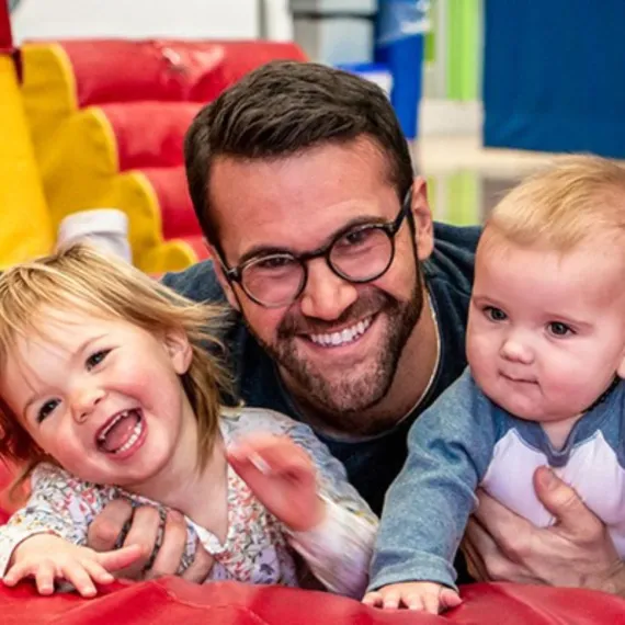 A father plays with his two toddler-aged children at a YMCA gym