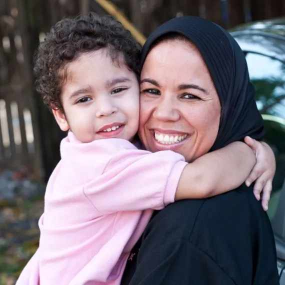 A woman and her young son embrace while smiling at the camera