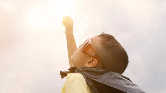 A young boy dressed as a superhero reaches toward the sky