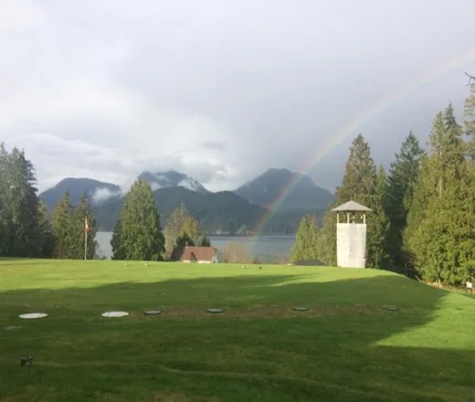 YMCA Camp Elphinstone's main field is pictured looking out towards Howe Sound. A rainbow arcs over the climbing wall.