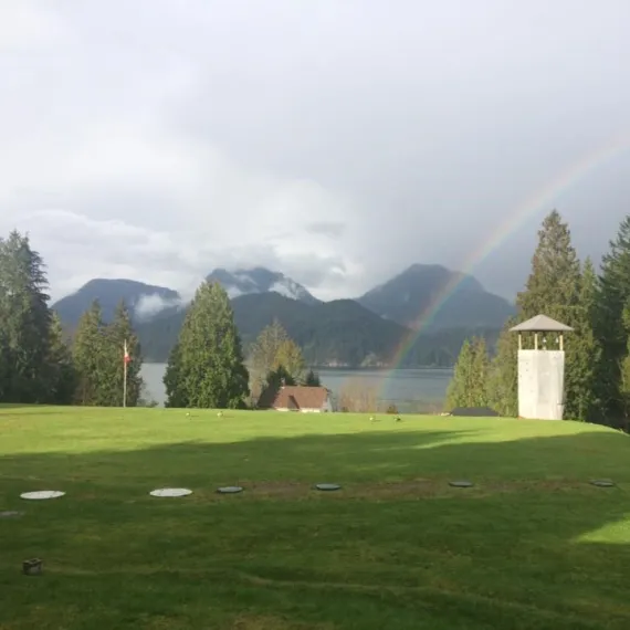 A view of the main field at Camp Elphinstone overlooking Howe Sound. A rainbow appears above the camp waterfront.