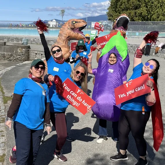 Energetic YMCA volunteers wear costumes and hold signs with encouraging messages along the BMO Vancouver Marathon route