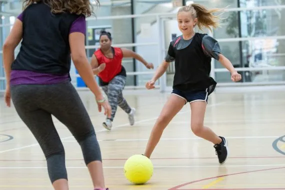 Three girls playing indoor soccer in a YMCA gynmasium
