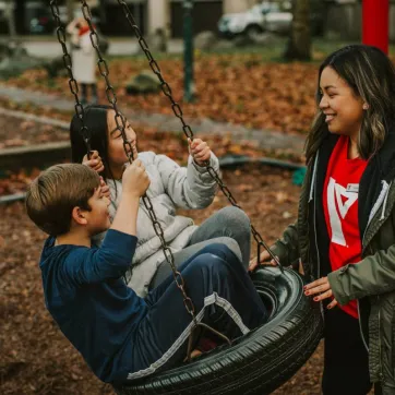 A YMCA BC child care staff member pushing two children on a tire swing