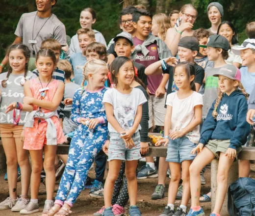 A group of children smile while singing songs at a campfire